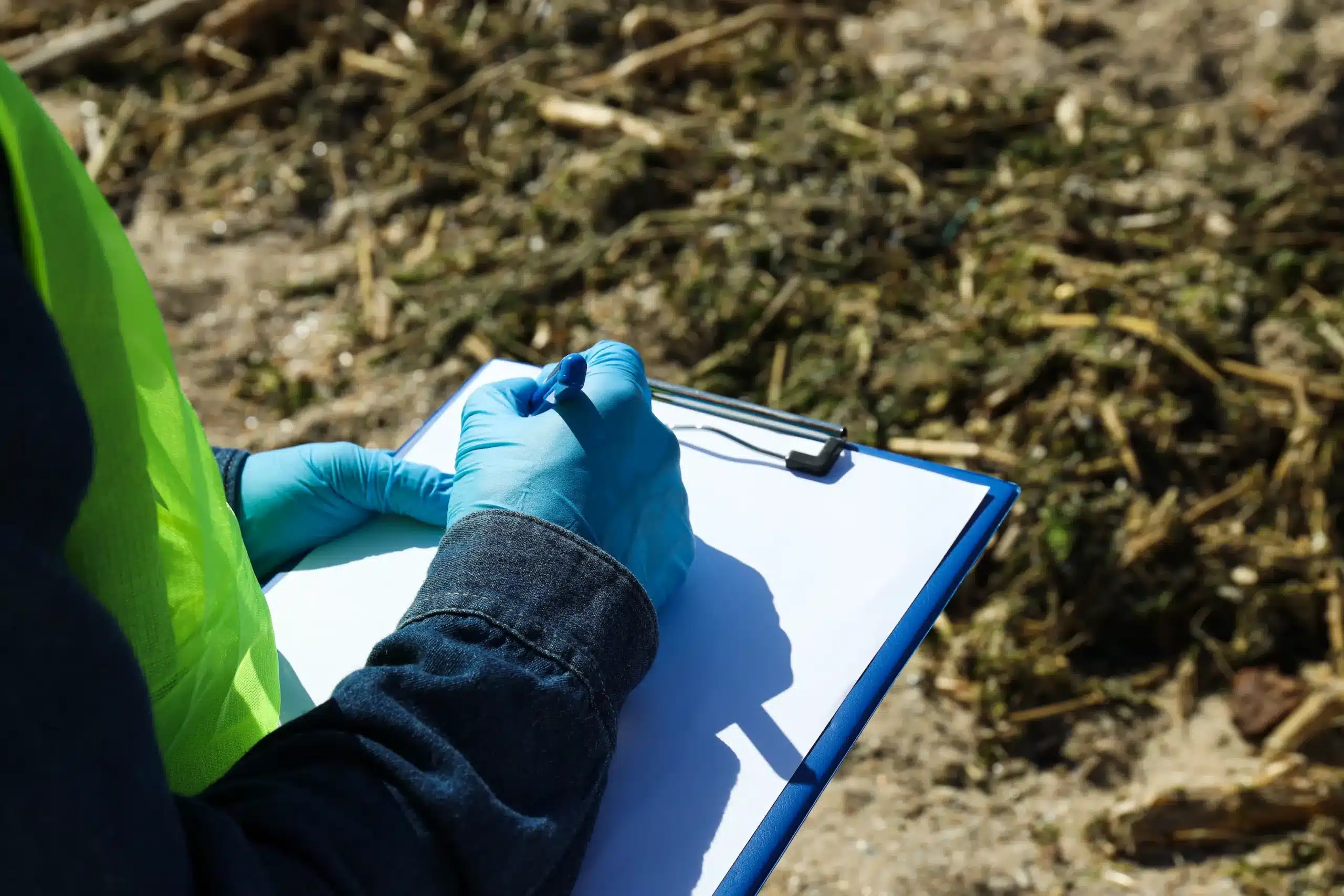 ingénieur en environnement sur un terrain de terre avec un gilet fluo est des gants de protection bleu qui écrit sur une feuille
