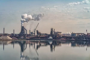 Aciérie en bord de mer avec hauts fourneaux, cheminées industrielles fumantes et stockage de minerai, vue depuis le quai