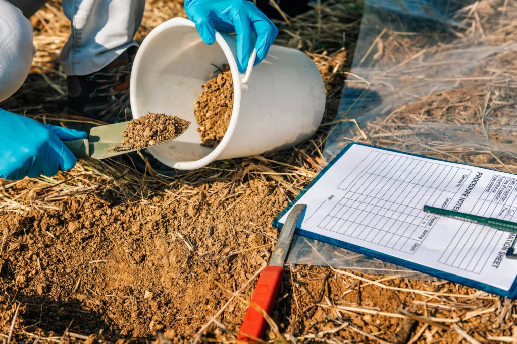 Ingénieur prélevant un échantillon de sol à la truelle pour analyse en laboratoire, avec fiche de traçabilité de prélèvement