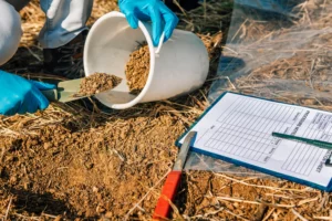 Ingénieur prélevant un échantillon de sol à la truelle pour analyse en laboratoire, avec fiche de traçabilité de prélèvement